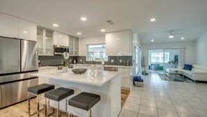 Een moderne keuken met een centraal eiland, roestvrijstalen apparatuur en een zithoek met een witte bank en salontafel.