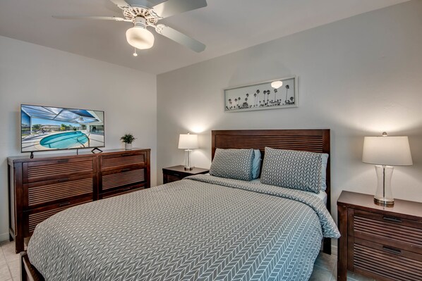A bedroom with a large bed, wooden headboard, two bedside tables with lamps, a ceiling fan, and artwork on the walls. - Villa Belle Isle - heated pool, south facing, cozy interior, close to river (Cape Coral)