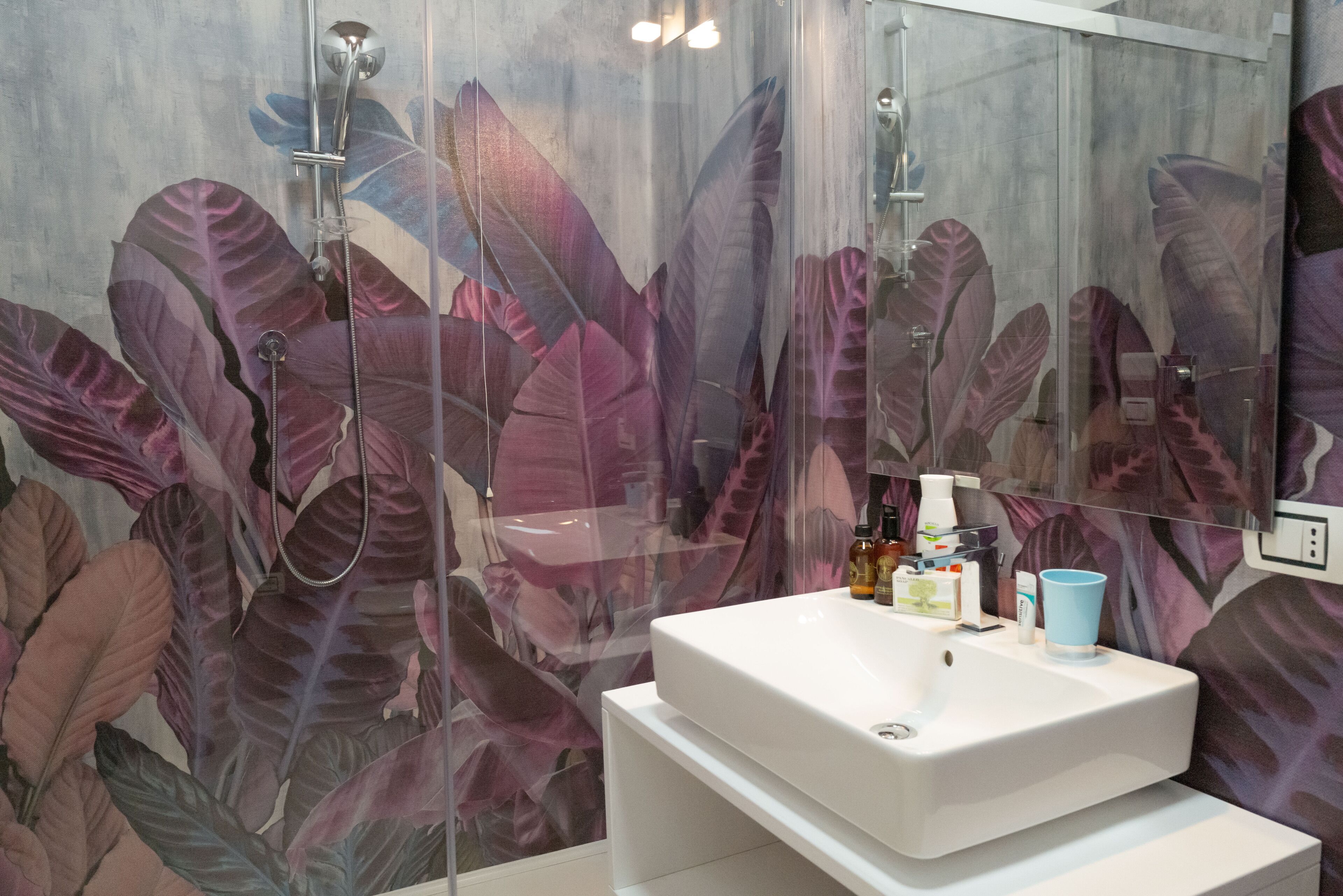 Un baño con un espejo grande, un lavamanos blanco y una ducha con puerta de cristal.
