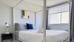 Ein Himmelbett mit weißer Bettwäsche, ein Nachttisch mit Lampe und ein Gemälde an der Wand.