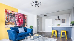 Een moderne woonkamer met een blauwe bank, een glazen salontafel en een levendig abstract schilderij aan de muur.