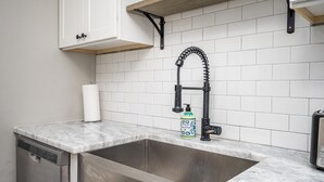 Een keuken met een RVS spoelbak, een marmeren aanrechtblad, een witte tegelachterwand, een zwarte kraan en een fles afwasmiddel.