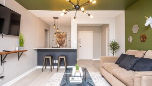 Ein modernes Wohnzimmer mit einem Glastisch, einem beigefarbenen Sofa und einer Küchenzeile mit Barhocker.