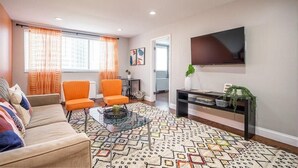 Een moderne woonkamer met een bank, twee fauteuils, een salontafel, een televisie en een kamerkleed met dessin.