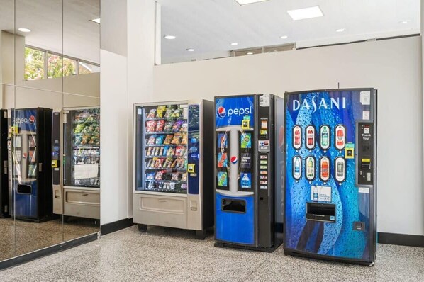 Drei Getränkeautomaten in einer Lobby mit Glaswand und Deckenleuchte.