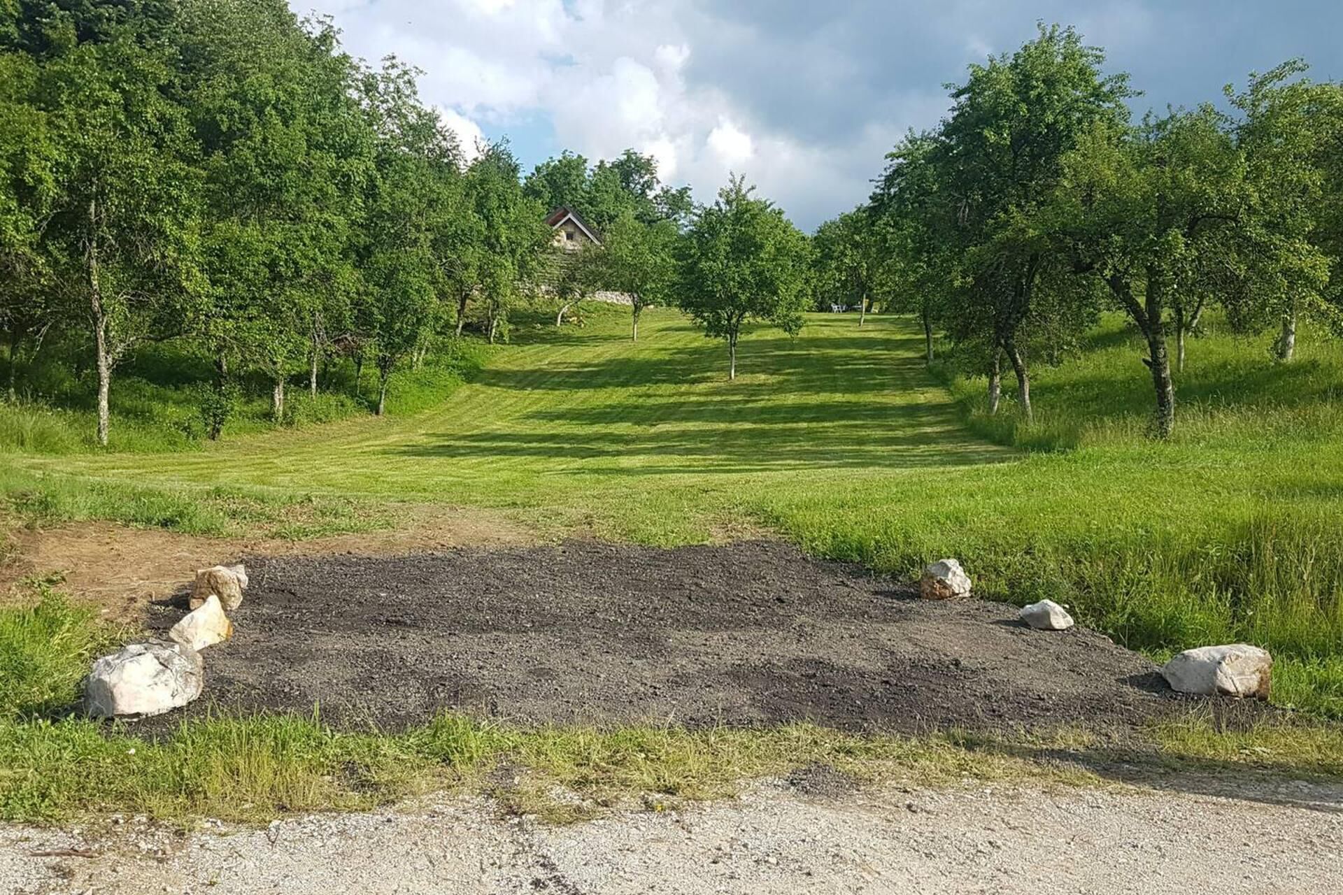 Paisagem rural com uma trilha de terra que leva a uma casa rodeada de árvores.