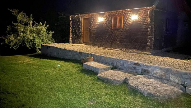 A stone building with a wooden door and window, illuminated by lights. - Charming 2bed Cottage in Carasova, Banat Mountains (Carasova)