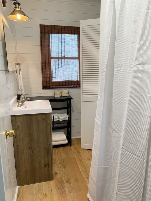 A bathroom with a wooden vanity, a white sink, a window with blinds, and a shower curtain.
