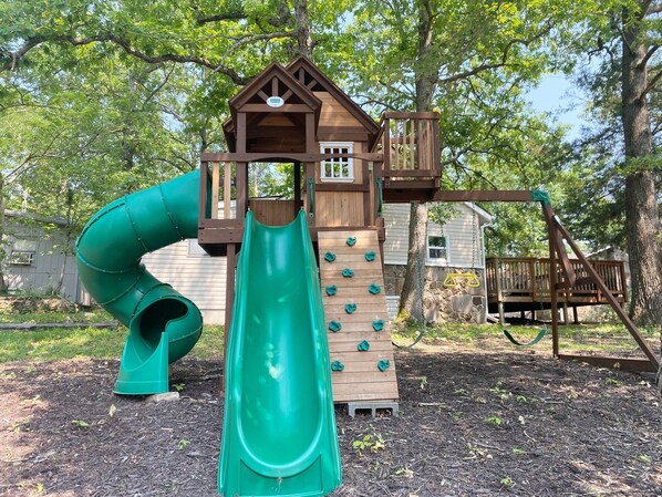 Explore the fun-filled play area with a green slide, climbing wall, and cozy wooden house.