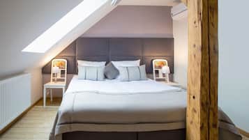 A bedroom with a sloped ceiling, a large bed with white bedding, two bedside tables with lamps, and a wooden headboard.