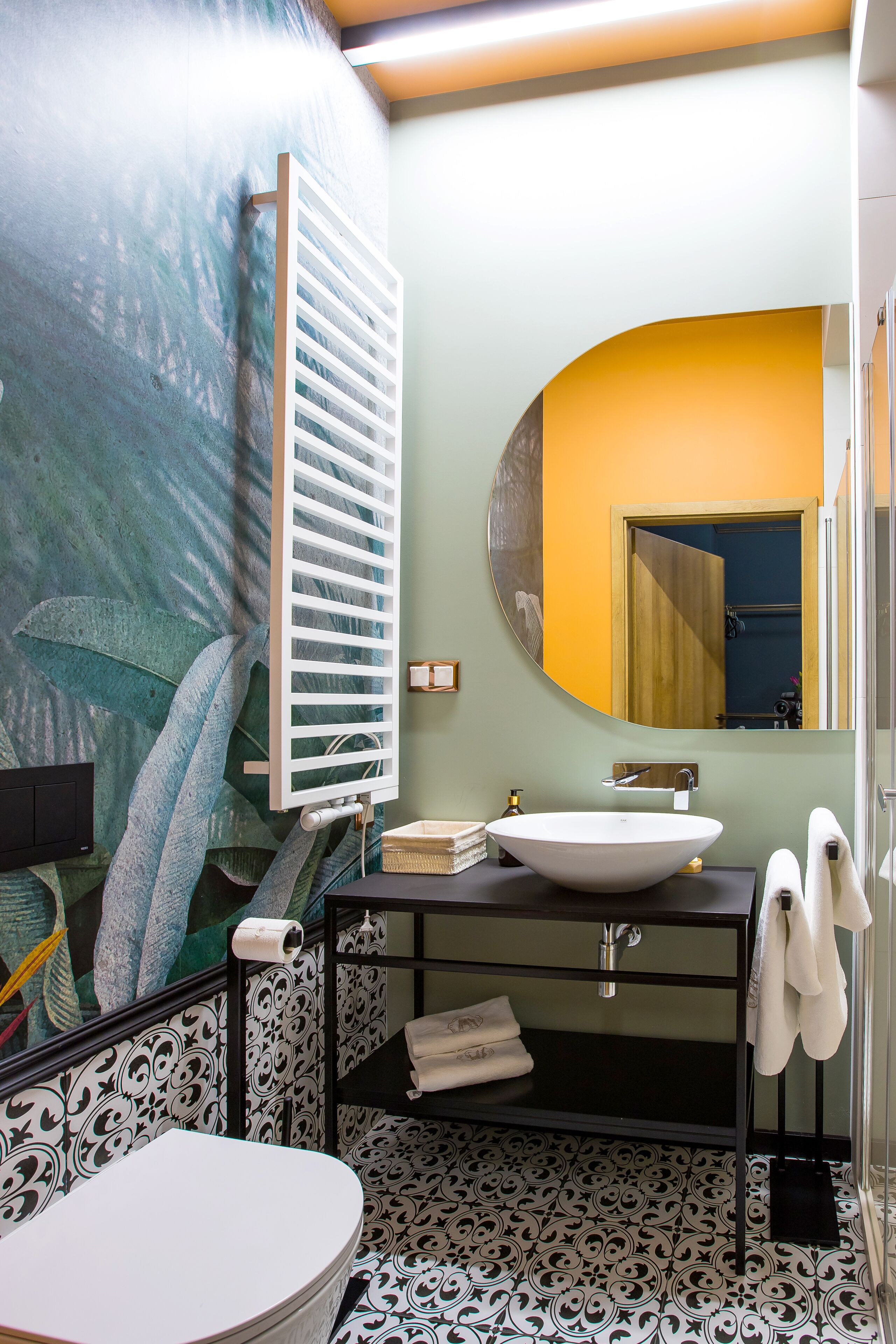 A bathroom with a large mirror, a white sink, a towel rack, and a toilet.