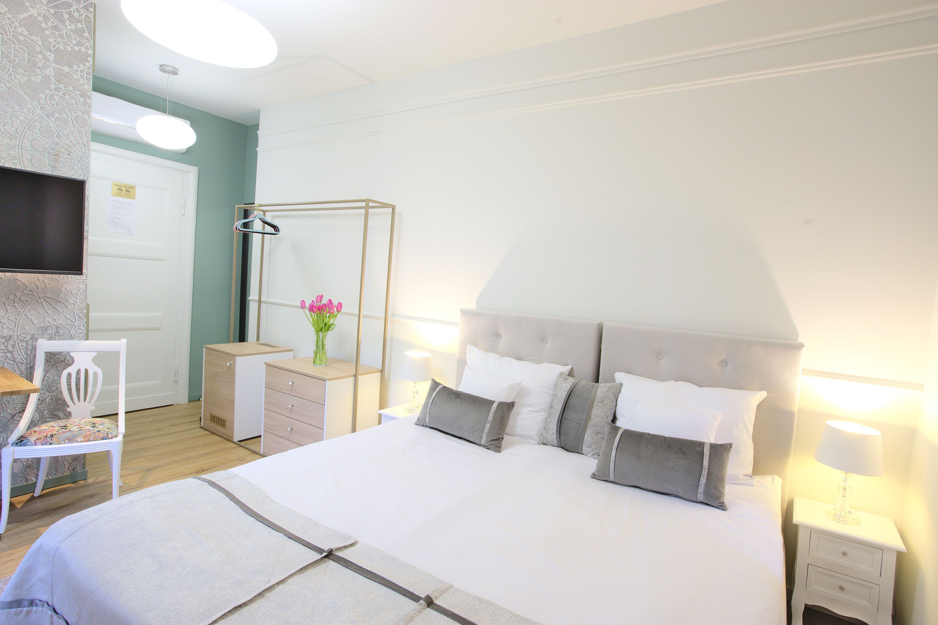 Quarto bem arrumado com uma cama grande, mesas de cabeceira, uma cadeira e uma televisão na parede.