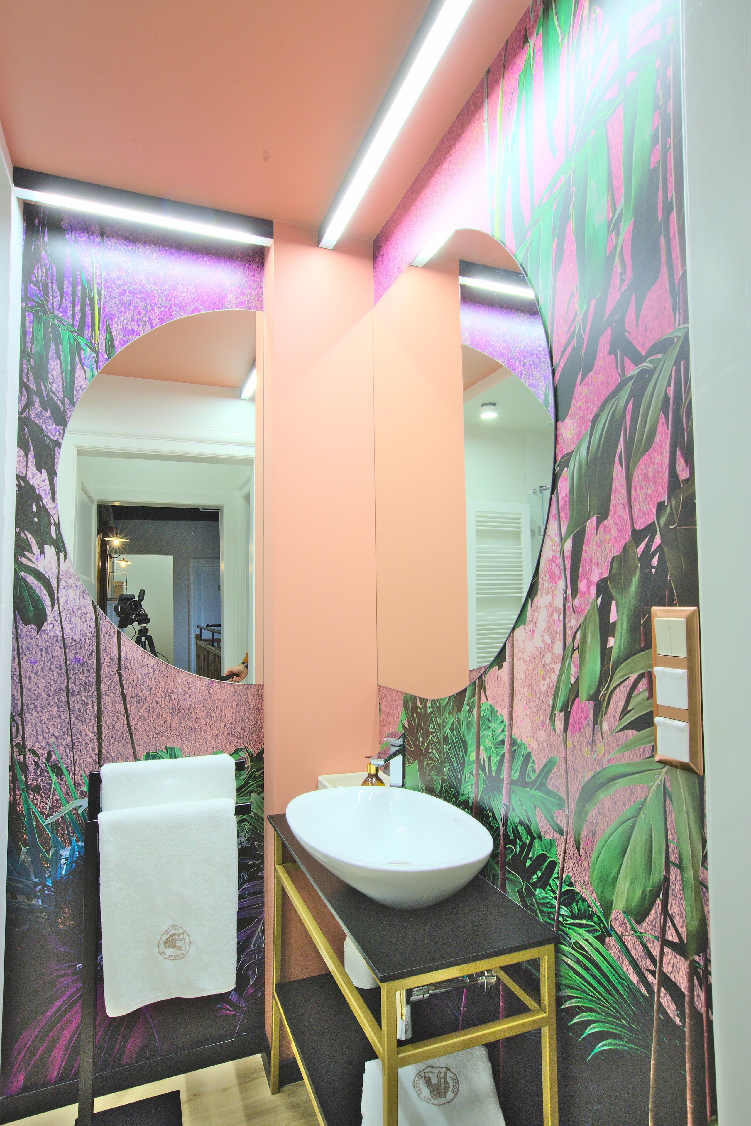 A bathroom with a round mirror, white sink, and a towel rack.