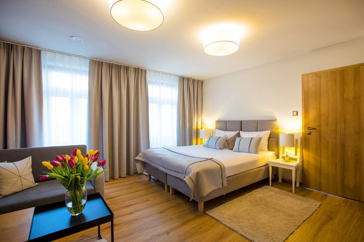 Hotellihuone, jossa on sänky, yöpöydät, sohva, maljakko täynnä kukkia ja puinen vaatekaappi.