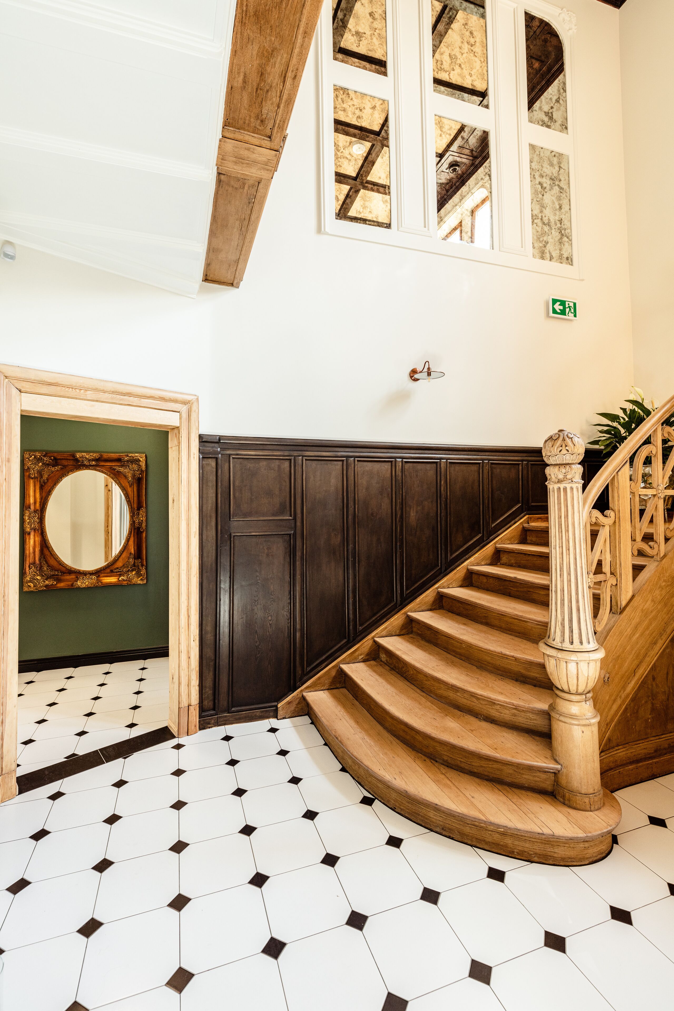 A staircase with wooden balusters and a handrail, leading to a landing with a green wall and a mirror.
