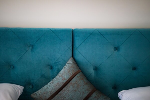 A teal upholstered headboard with a diamond pattern and buttons, flanked by white pillows.