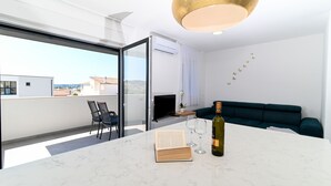 En moderne stue med en glasdør til en balkon, en grøn sofa, et marmorbord med en bog og vinglas, samt en loftlampe.