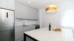 Et moderne køkken med stålemmer, en marmorbordplade og en hængende lampe.