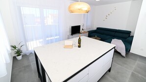 En moderne stue med en stor ø, en grøn sofa, et fjernsyn og en hængende lampe.
