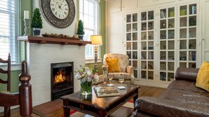 A cozy living room with a fireplace, a comfortable armchair, a leather sofa, and a bookshelf filled with books. - Magnolia Manor and Chapel (Humboldt)