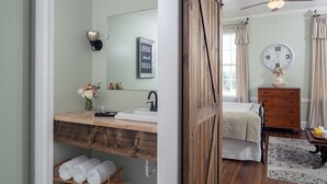 A bedroom with a wooden vanity, a bed, a dresser, a clock, and a window with curtains. - Magnolia Manor and Chapel (Humboldt)