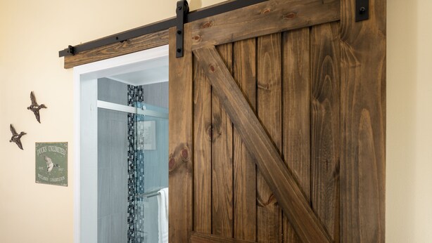 A wooden barn-style door leading to a bathroom with a glass shower enclosure. - Magnolia Manor and Chapel (Humboldt)