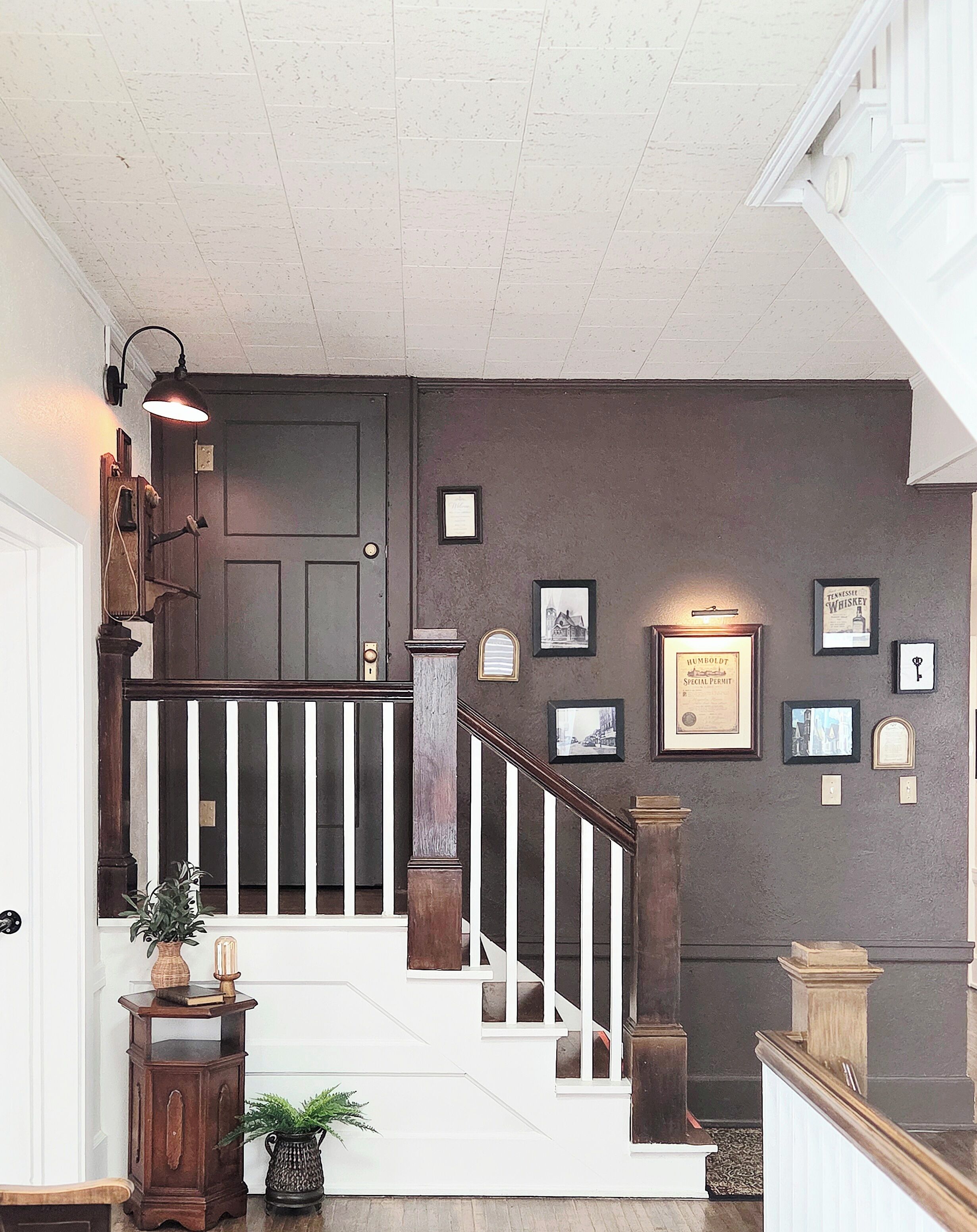 A staircase with a white railing, a dark door, and a wall adorned with framed pictures and certificates.