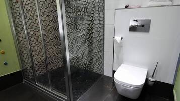 Een badkamer met een douchecabine van glas, een wit toilet en een betegelde wand.