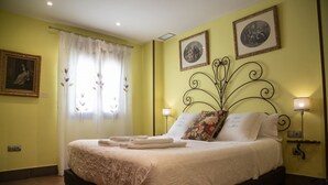 Een netjes opgemaakt bed met een bloemenprint deken en kussens, een bedlampje en een lijst met een foto aan de muur.