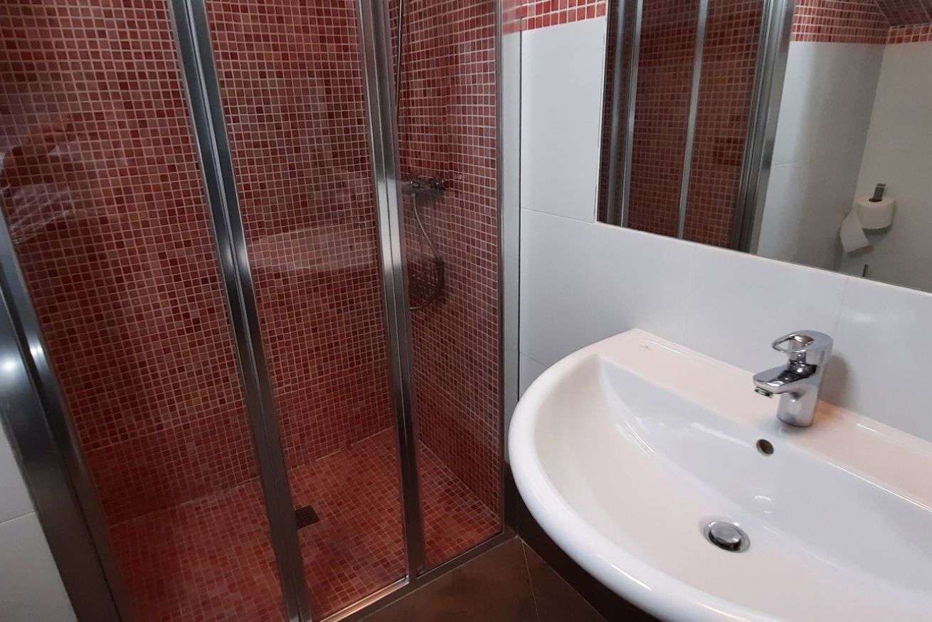 Un baño con cabina de ducha de vidrio, un lavabo blanco y un espejo.