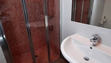 Un baño con cabina de ducha de vidrio, un lavabo blanco y un espejo.