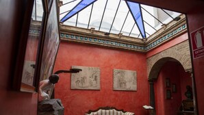A room with a red wall, a wooden bench, and two framed artworks.