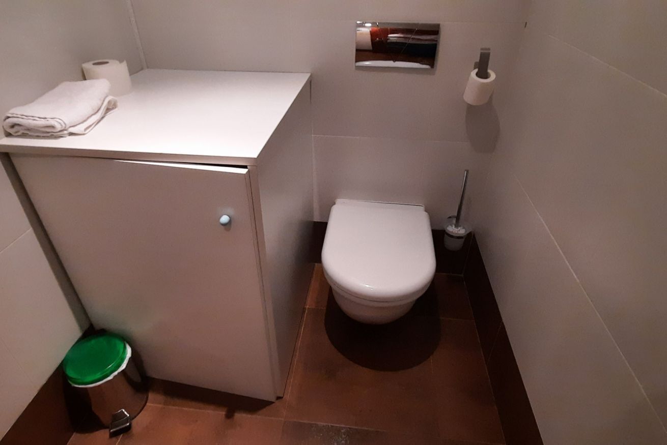 Een kleine badkamer met toilet, wastafel, prullenbak en een handdoek op het aanrecht.