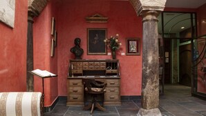 A lobby with a red wall, a wooden desk, a bust sculpture, and a vase of flowers.