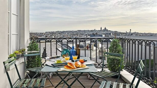Ein Balkon mit Frühstückstisch, der auf eine Stadtansicht und ein Gewässer blickt.
