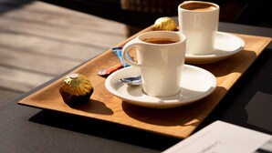 Un vassoio con due tazze di caffè, un pasticcino e una borsa su un tavolo vicino a una piscina.