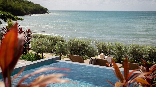 Vista della piscina con spiaggia oceanica e paesaggio verdeggiante.