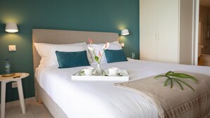 A neatly made bed with a tray of breakfast items, including a vase with flowers, in a hotel room with teal walls and white furniture. - Villa Orlov - Luxury villa on the water (Le Diamant)
