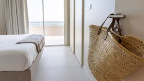 Una camera d'albergo con un letto, un cesto di vimini e vista sulla spiaggia tramite una porta scorrevole.