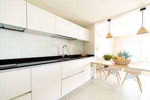 Une cuisine moderne avec des meubles blancs, un plan de travail noir et un coin repas comprenant des chaises en bois et un panier de fruits.