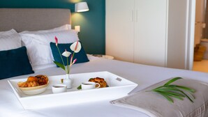 Ein ordentlich bezogenes Bett mit einem Frühstücksbrett, das Croissants, Kaffeetassen und eine Vase mit Blumen enthält.