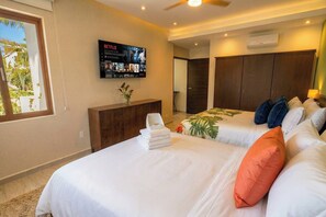 Habitación de hotel con dos camas, un televisor montado en la pared mostrando Netflix, un armario de madera y una ventana con vista a palmeras.