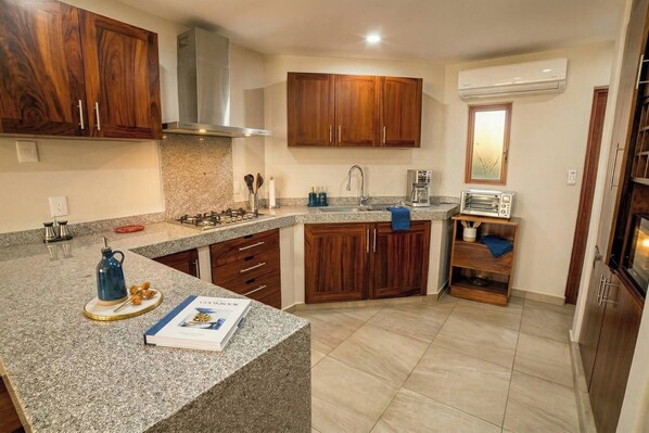 Una cocina con encimeras de granito, armarios de madera, estufa a gas y un equipo de aire acondicionado.