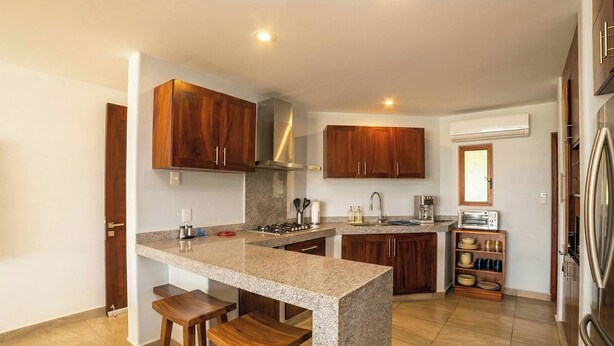 Una cocina moderna con encimeras de granito, armarios de madera, horno empotrado y refrigerador de acero inoxidable.