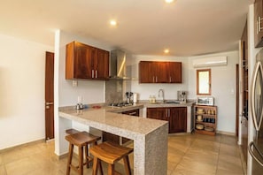 A modern kitchen with granite countertops, wooden cabinets, a built-in oven, and a stainless steel refrigerator.