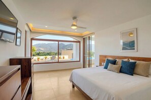 A bedroom with a large bed, a ceiling fan, a view of mountains, and a balcony with plants. - El Tular 002 at El Tular | Pool + Prime Location (Zihuatanejo)