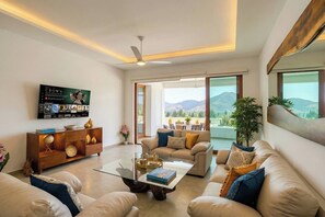 A modern living room with a sofa set, a coffee table, a TV mounted on the wall, and a view of the outdoors. - El Tular 002 at El Tular | Pool + Prime Location (Zihuatanejo)