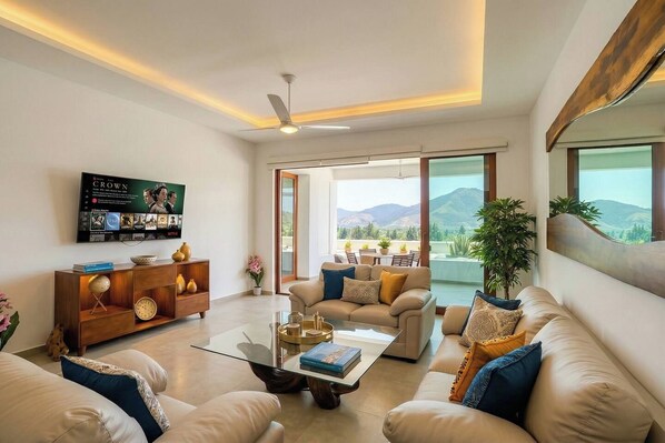 A modern living room with a sofa set, a coffee table, a TV mounted on the wall, and a view of the outdoors.