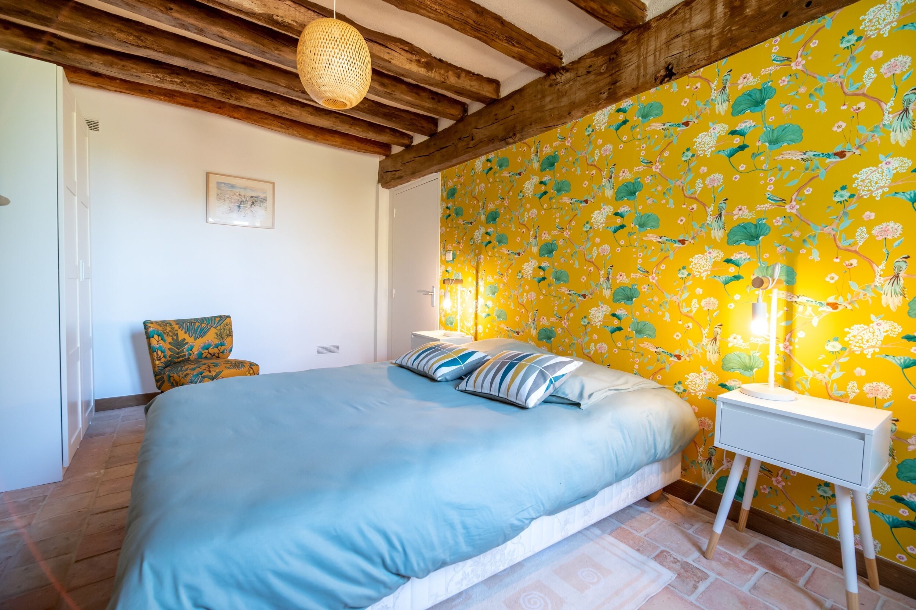 A bedroom with a bed, a nightstand, a chair, and a wooden ceiling.