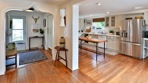 A spacious kitchen with wooden flooring, white cabinetry, and a stainless steel refrigerator.